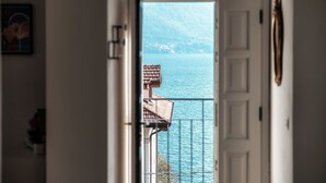 Blick durch eine Tür auf einen Balkon mit Blick auf ein Gewässer, im Hintergrund sind Gebäude zu sehen.