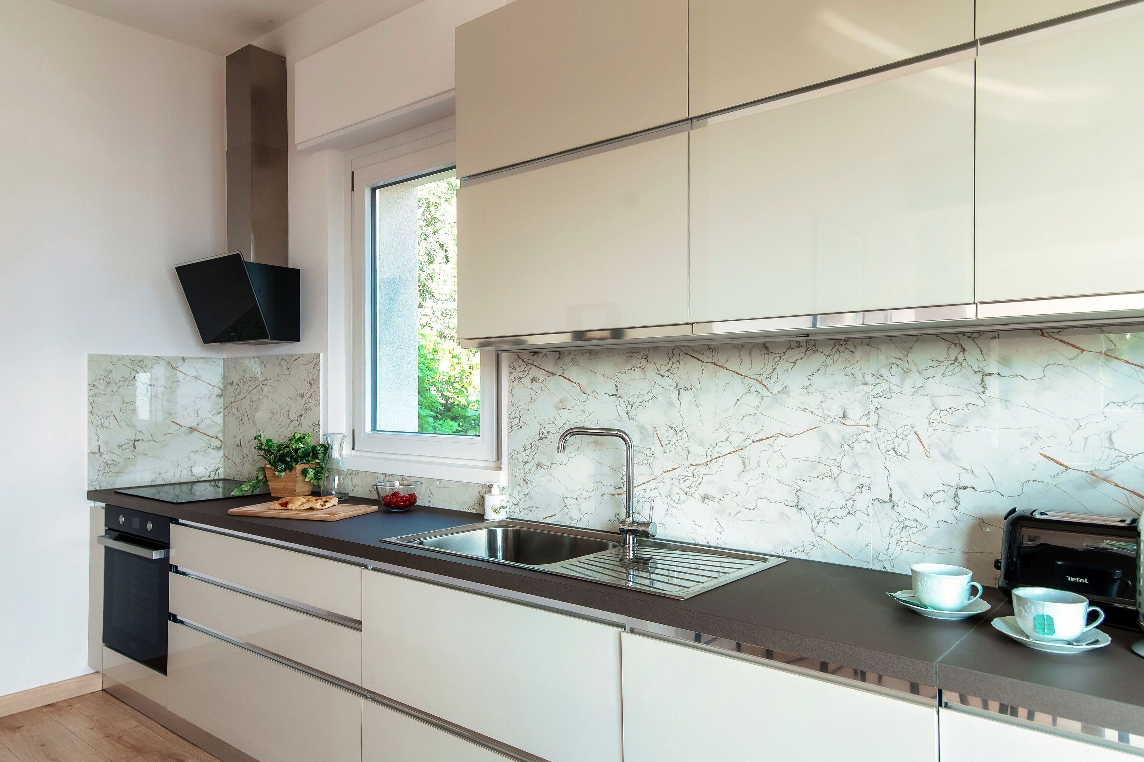 A modern kitchen with a marble backsplash, stainless steel appliances, and a window providing natural light.