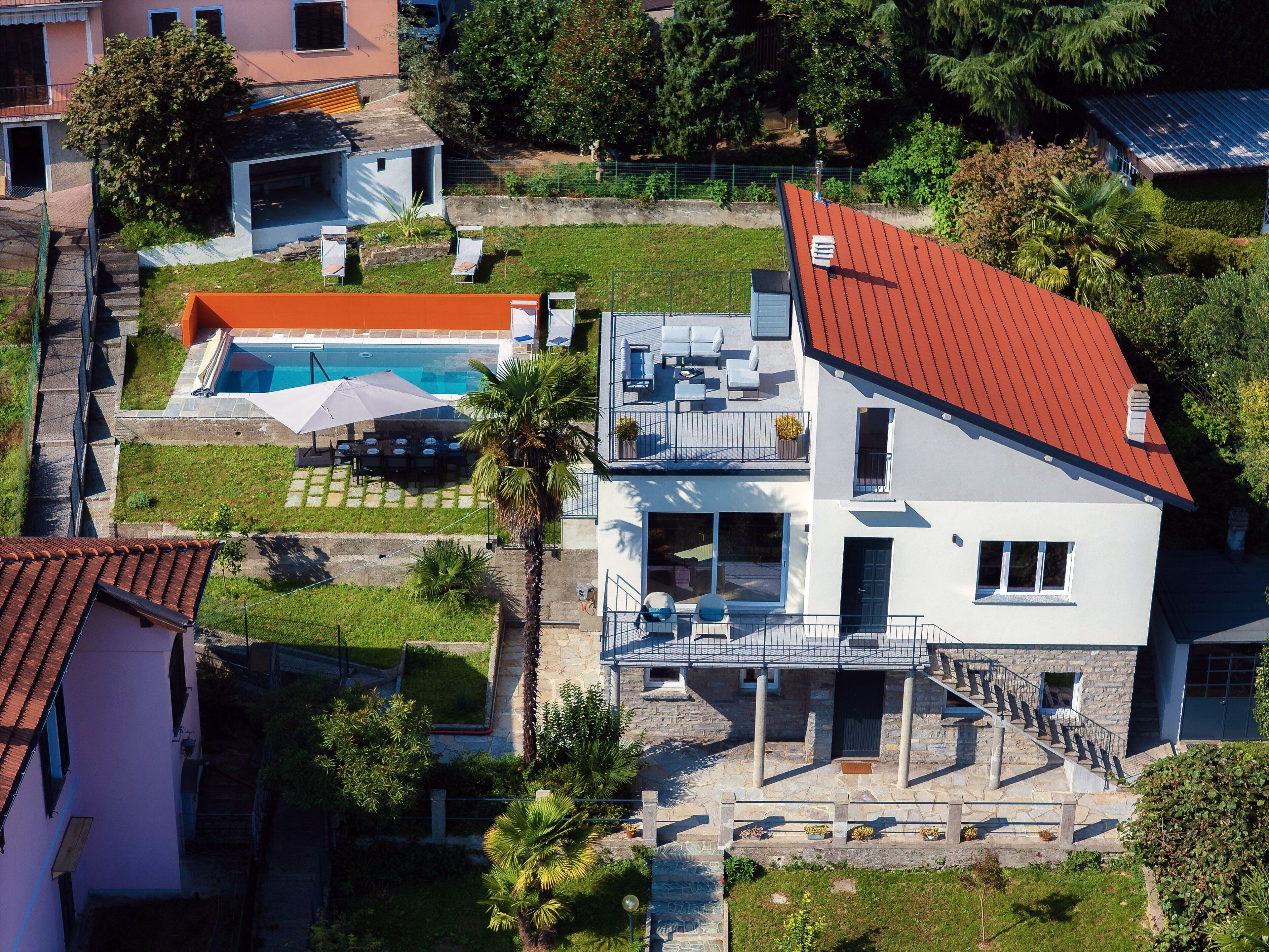 A two-story house with a swimming pool, outdoor seating, and a stone staircase.