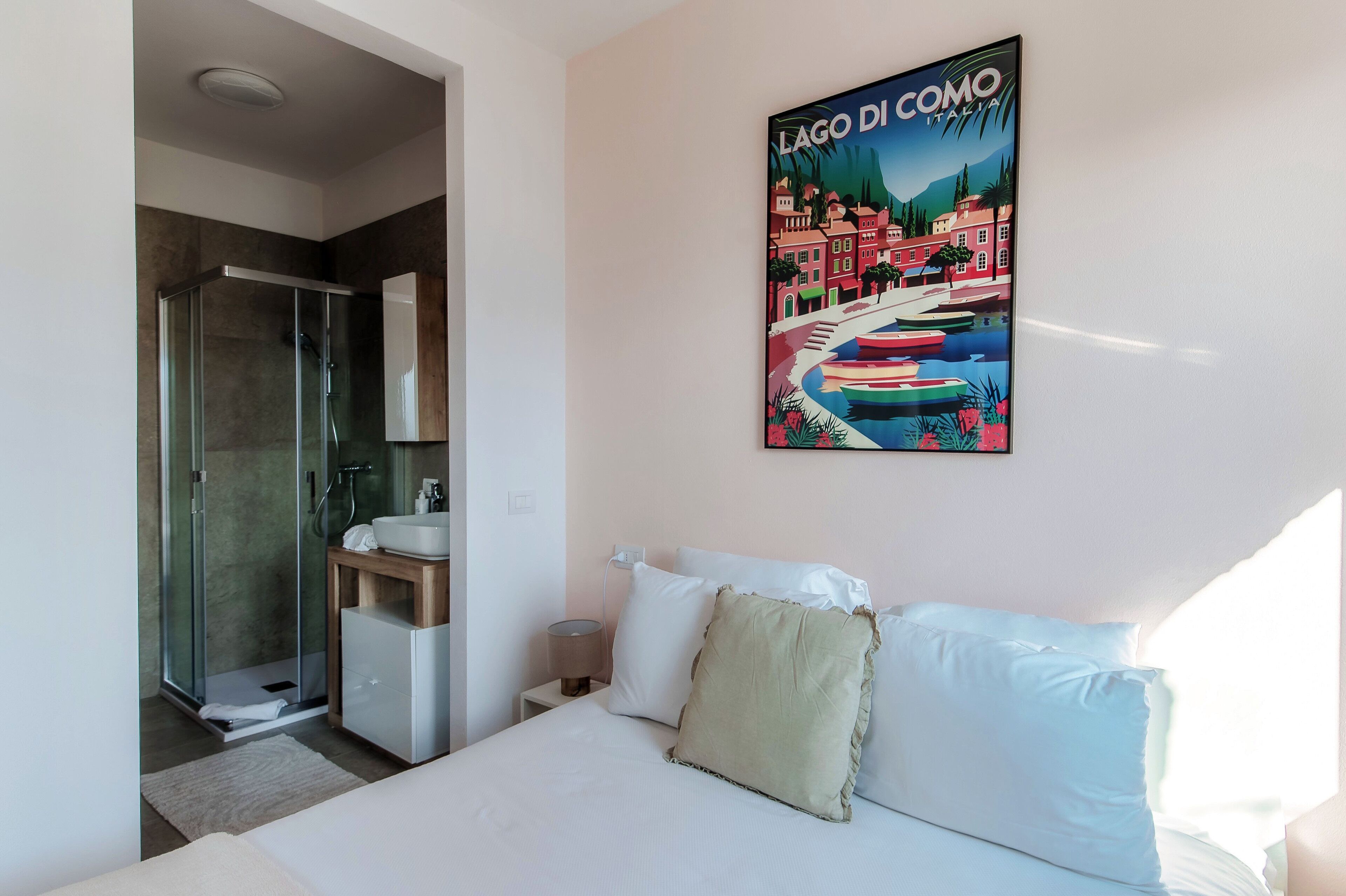 Una habitación de hotel con una cama, ducha, lavamanos y un cartel que muestra una escena de pueblo.