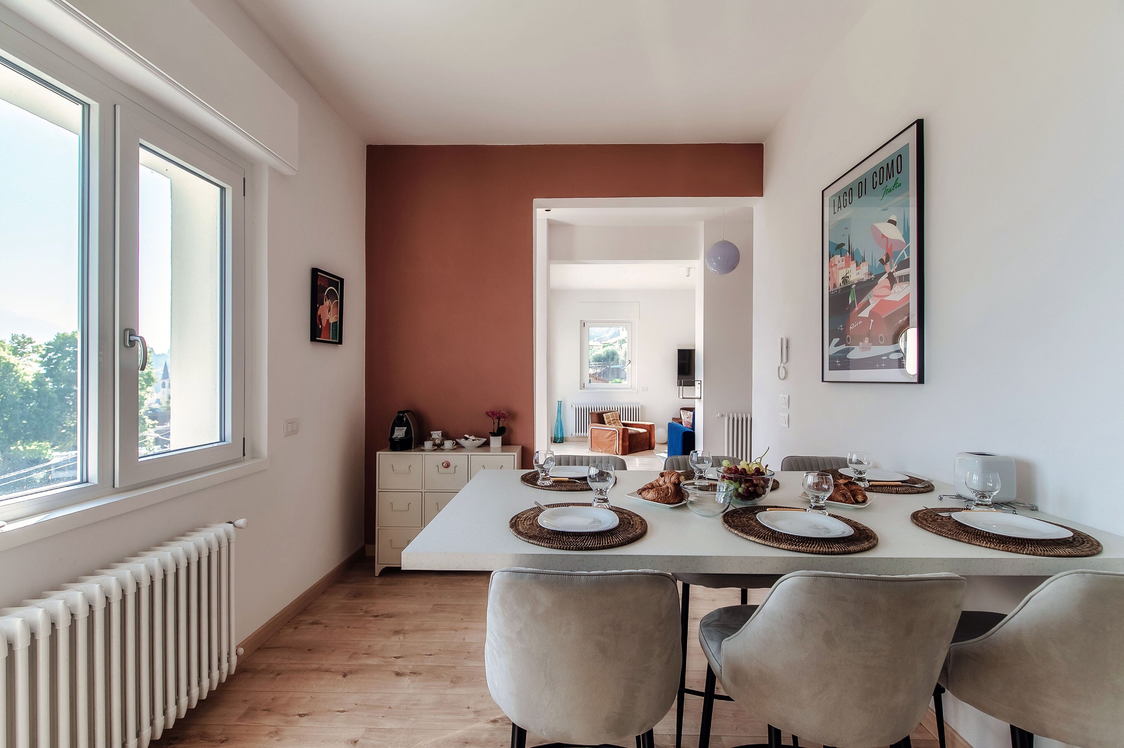 Comedor con una mesa blanca preparada para cuatro, un radiador y vistas a través de una ventana.