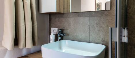 A bathroom with a white sink, wooden countertop, beige curtains, a mirror, and a shower area.
