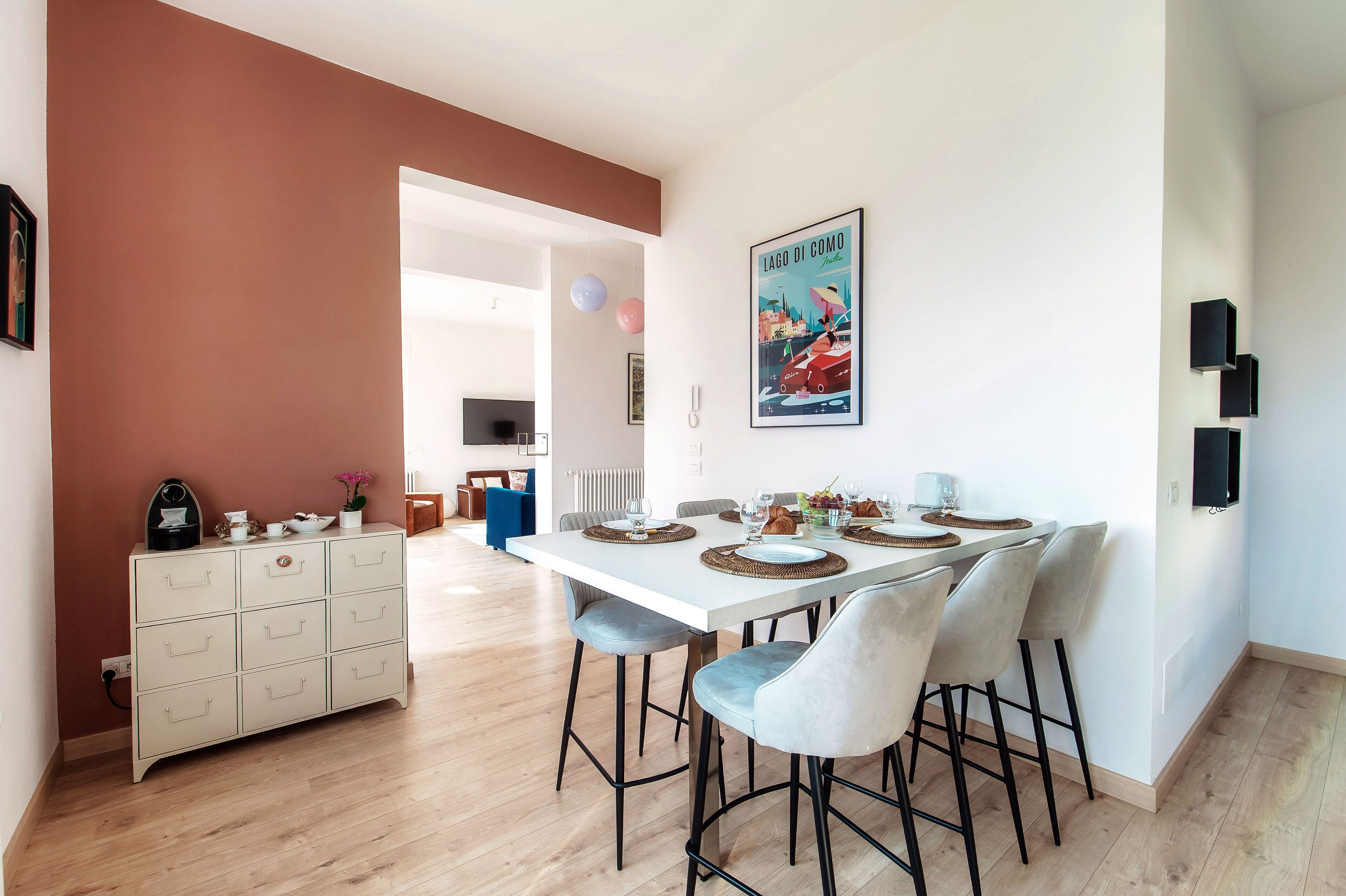 A modern dining area with a white table set for four, light blue chairs, and a white cabinet with drawers.