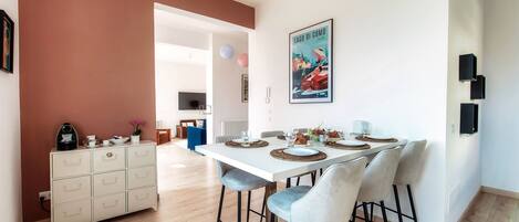 A modern dining area with a white table set for four, light blue chairs, and a white cabinet with drawers.