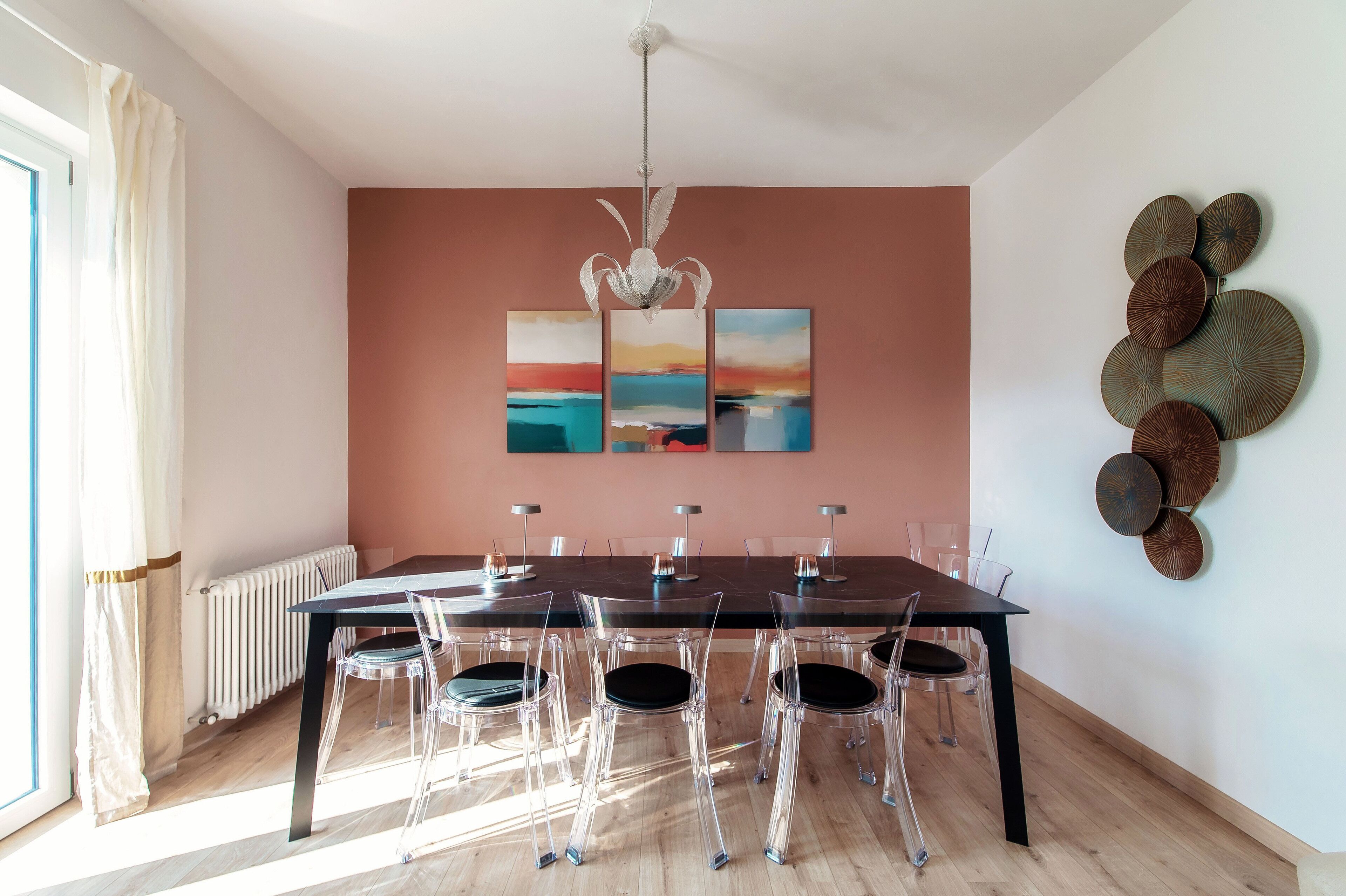A dining area with a table set for six, clear chairs, a radiator, and wall art.