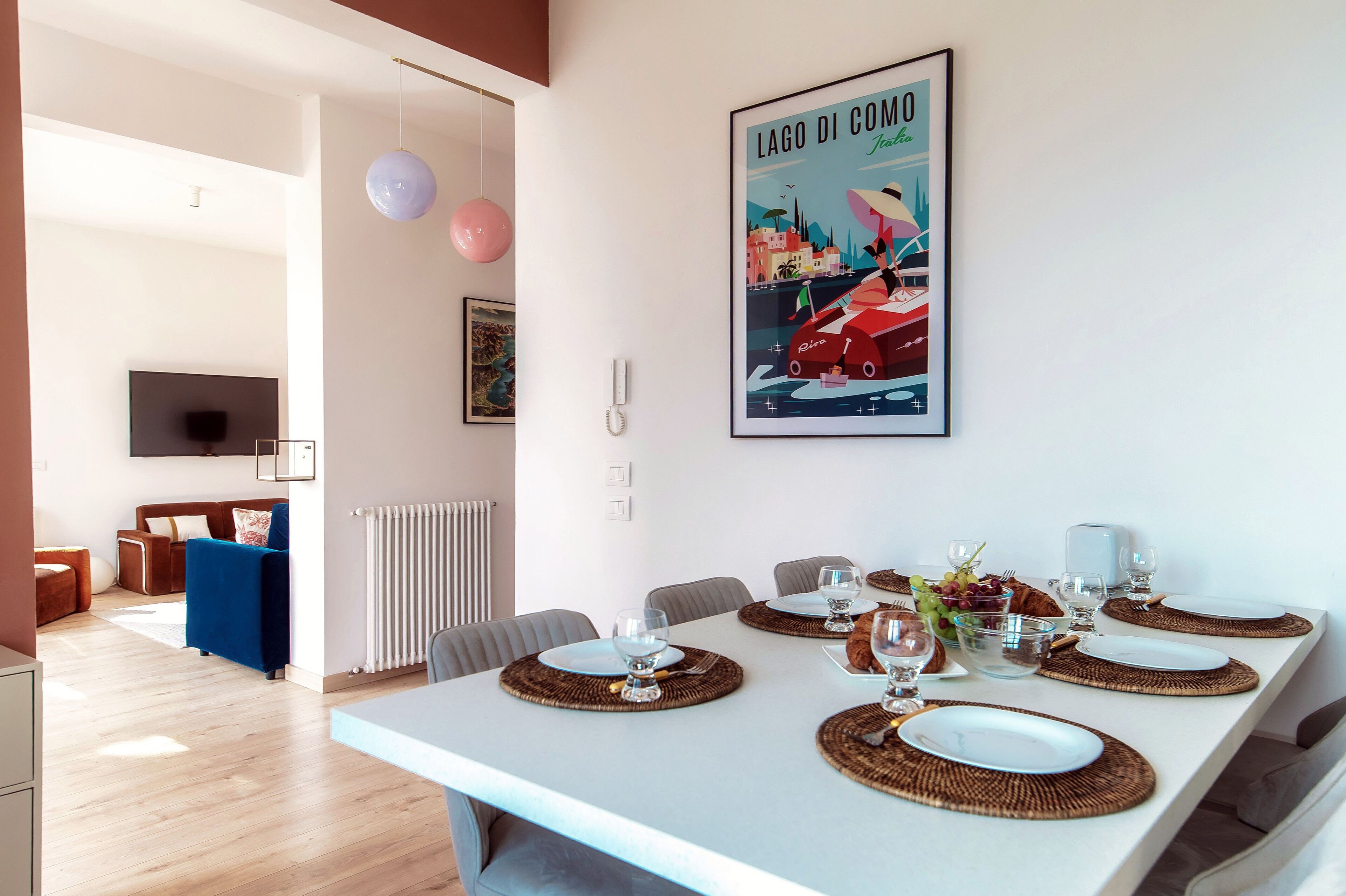 Un comedor moderno con una mesa larga dispuesta para cuatro personas, un cuadro colgado de un barco y un radiador blanco.