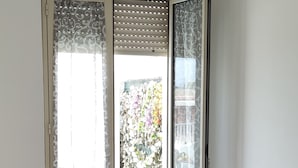 A bedroom with a bed, a nightstand with a lamp, a ceiling fan, and a view through a window with patterned curtains. - Apartment with terrace a few steps from the sea (San Lorenzo)