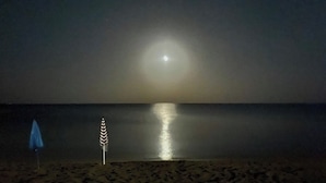 A beach at night with a visible moon reflection on the water, a blue umbrella, and a striped umbrella. - Apartment with terrace a few steps from the sea (San Lorenzo)