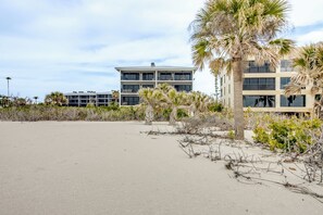 Ein Hotel direkt am Strand mit mehreren Etagen, Palmen und einem Sandstrand.