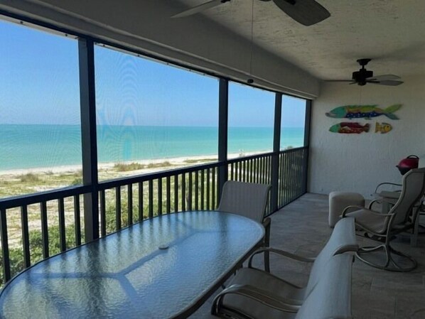 Ein Balkon mit Glastisch und Stühlen mit Blick auf einen Strand.