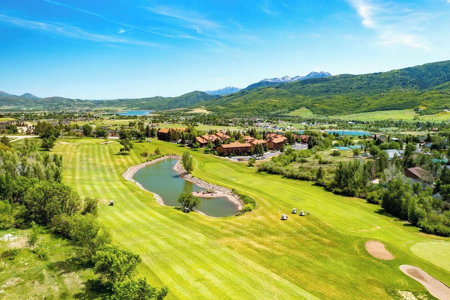 Een golfbaan met een vijver, omgeven door woongebouwen en bergen op de achtergrond.