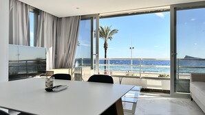 A modern hotel room with a balcony overlooking a beach, a large TV, and a table with a remote control.