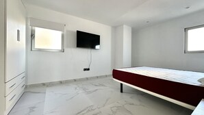A bedroom with a bed, a TV mounted on the wall, and a window.