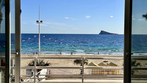 A beach view with a clear sky, a rocky outcrop in the distance, and a railing in the foreground.