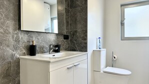 A modern bathroom with a marble backsplash, a white sink, a mirror, and a toilet.