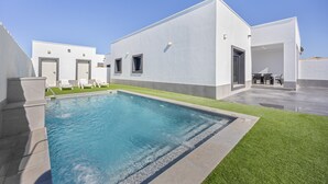 A modern building with a swimming pool, a patio with chairs, and a clear sky.