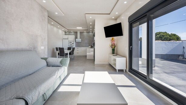 A modern interior with a sofa, a dining area, a kitchen, and a large window.