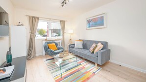 A modern living room with a grey sofa, a blue armchair, a glass coffee table, and a colorful striped rug.