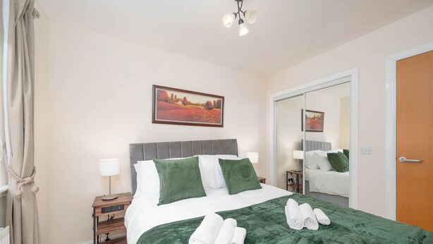 A hotel room with a bed, a nightstand, a mirror, and a painting on the wall.