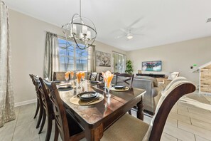 A dining area with a wooden table set for four, a chandelier, and a ceiling fan. - Gorgeous 5Bd w Pool Lazy River Storey Lake 4989 (Kissimmee)