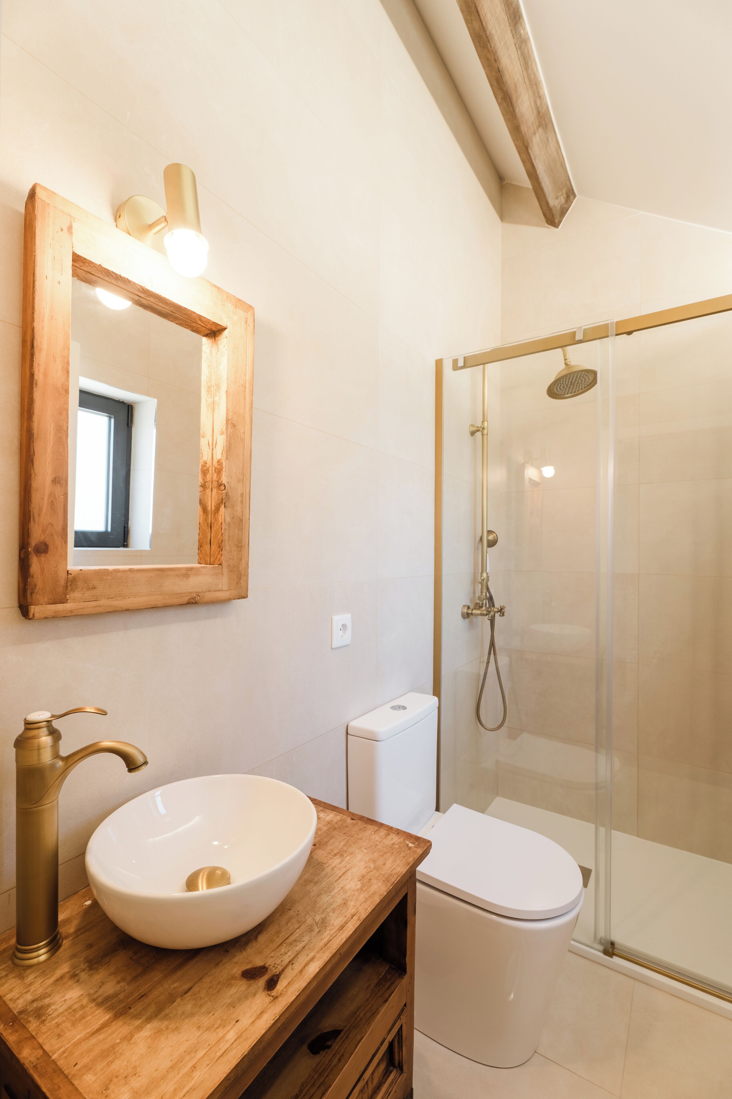 Een badkamer met een houten wastafelmeubel, een witte wasbak, een toilet en een douche met glazen wand.