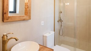 Een badkamer met een houten wastafelmeubel, een witte wasbak, een toilet en een douche met glazen wand.