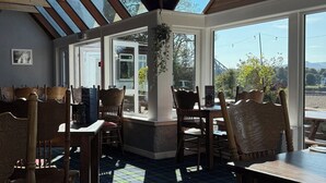 A restaurant with a high ceiling and skylights, wooden beams, and a view of the outdoors.