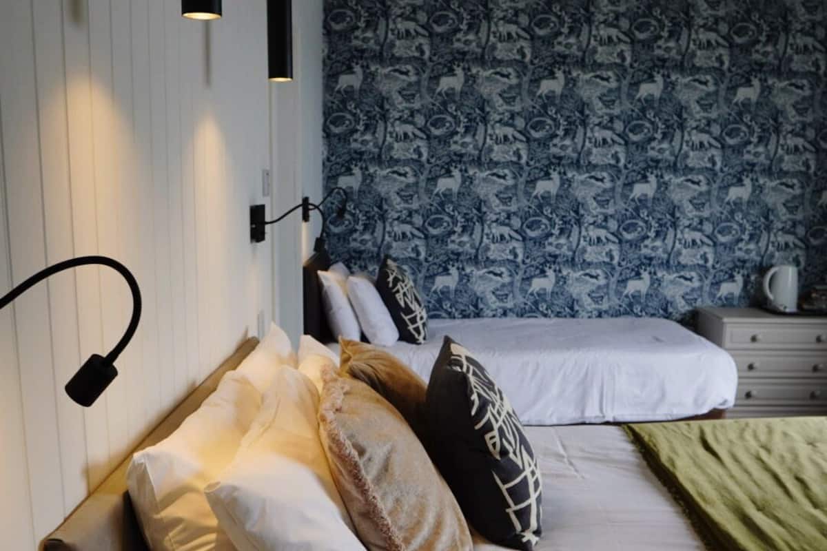 Ett hotellrum med två sängar, ett nattduksbord, en lampa och en tapet med mönster.