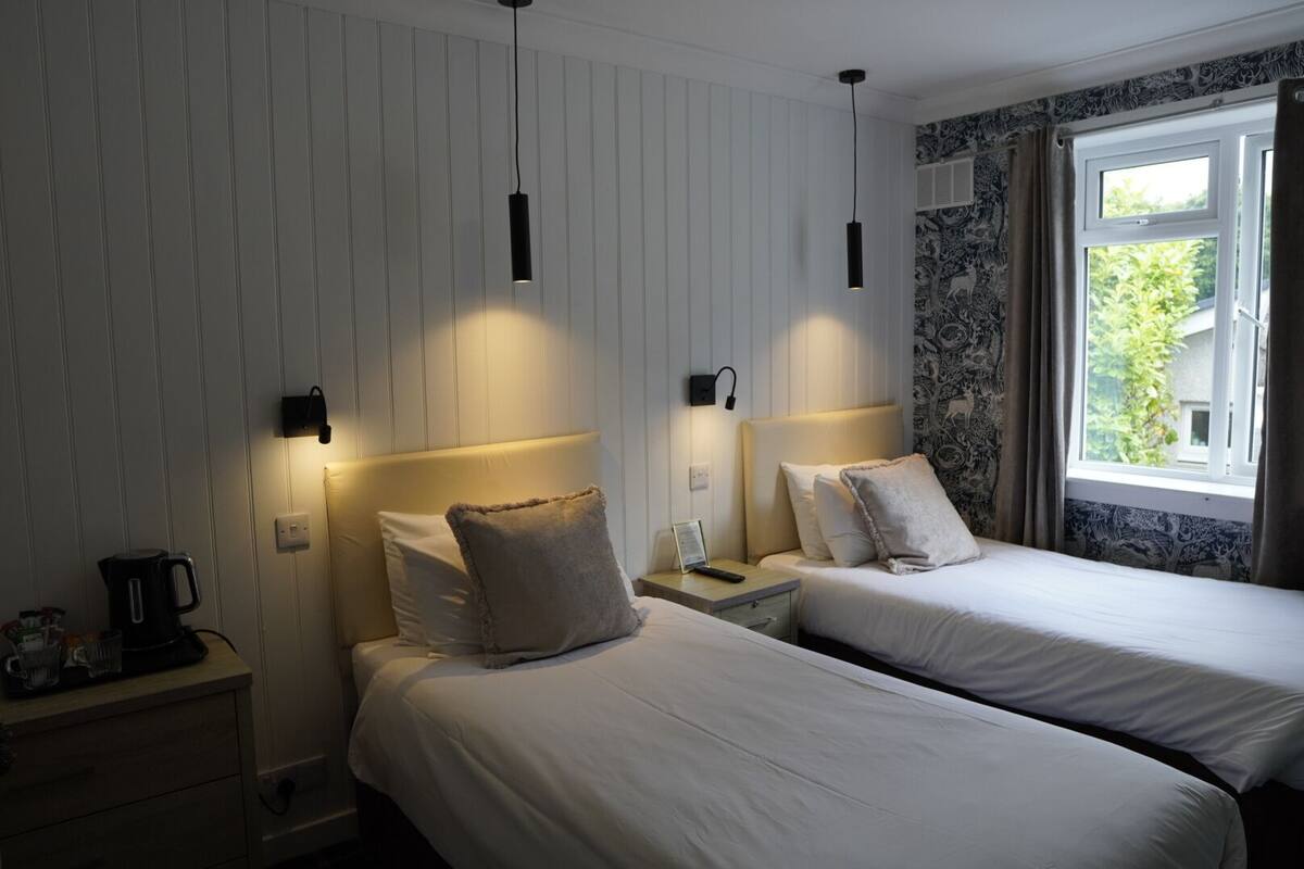 Ett hotellrum med två sängar, ett nattduksbord, en vattenkokare och ett fönster med gardiner.