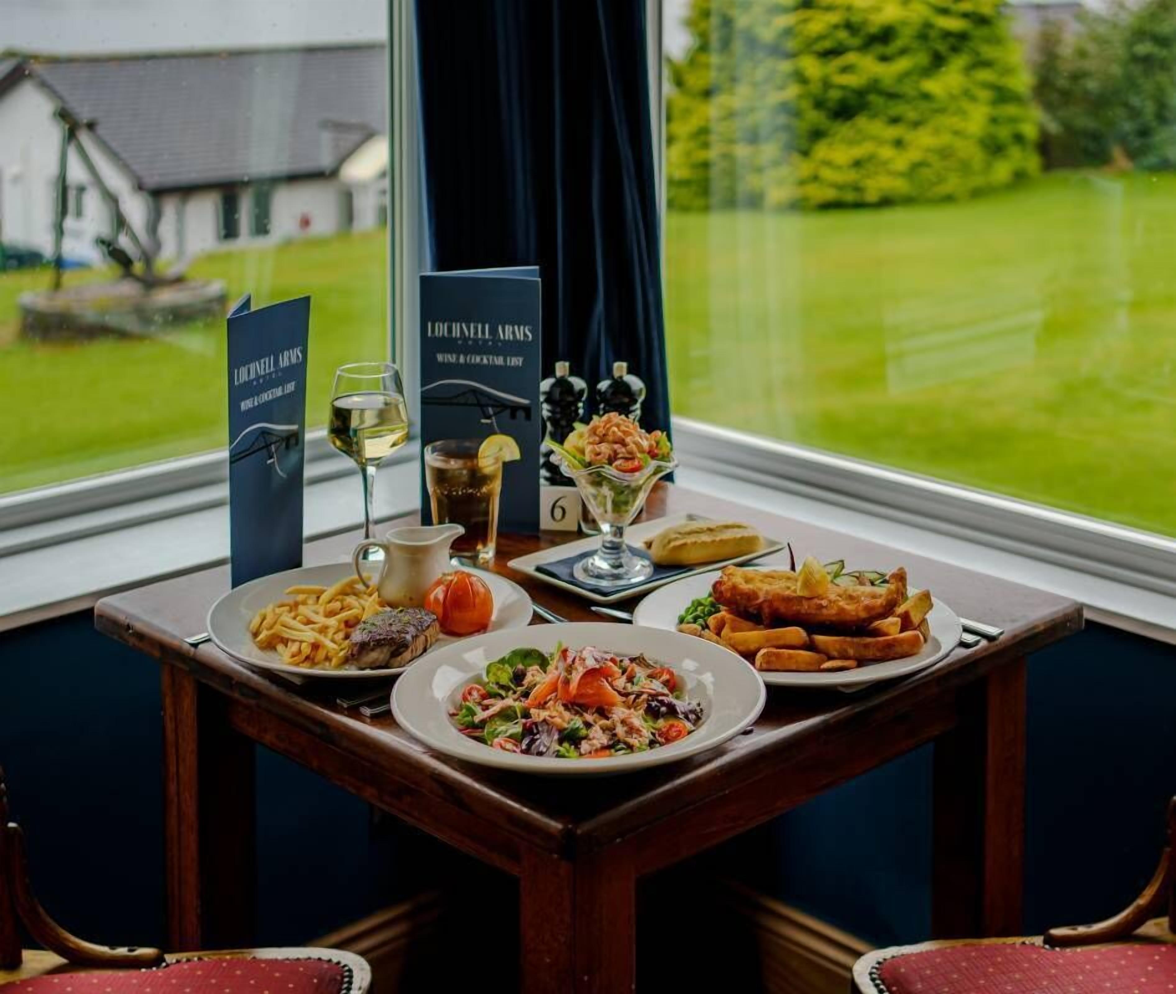 Une table avec un menu, un verre à vin et des assiettes de nourriture, notamment du poisson et de la salade.