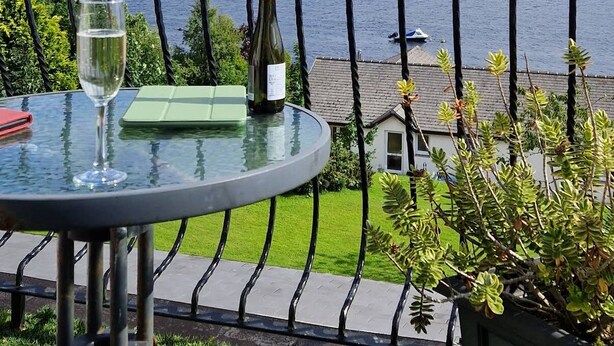A table with a glass of water and a bottle, overlooking a lake with houses in the background.