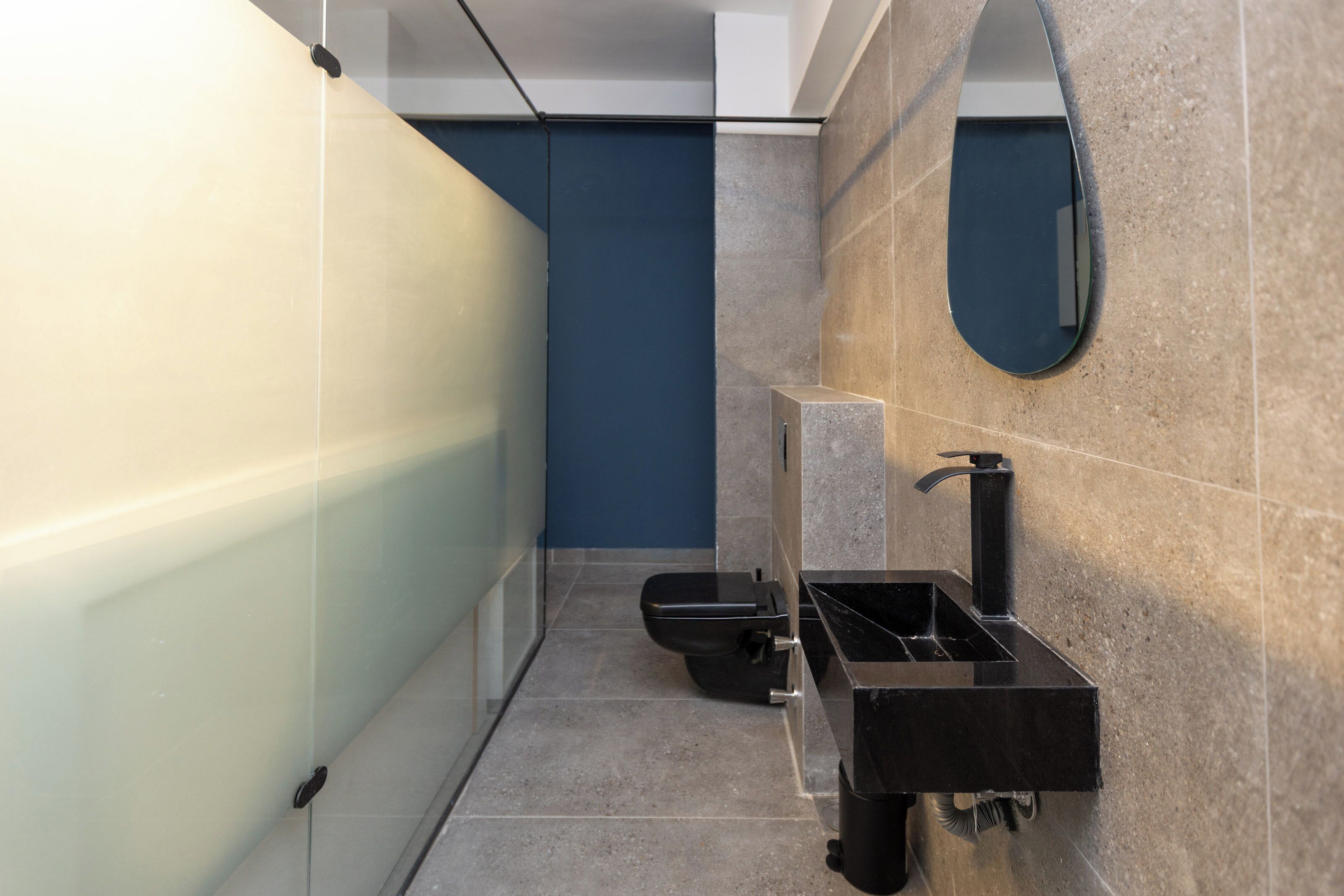 Une salle de bain moderne avec une paroi en verre, un lavabo noir et un miroir mural.