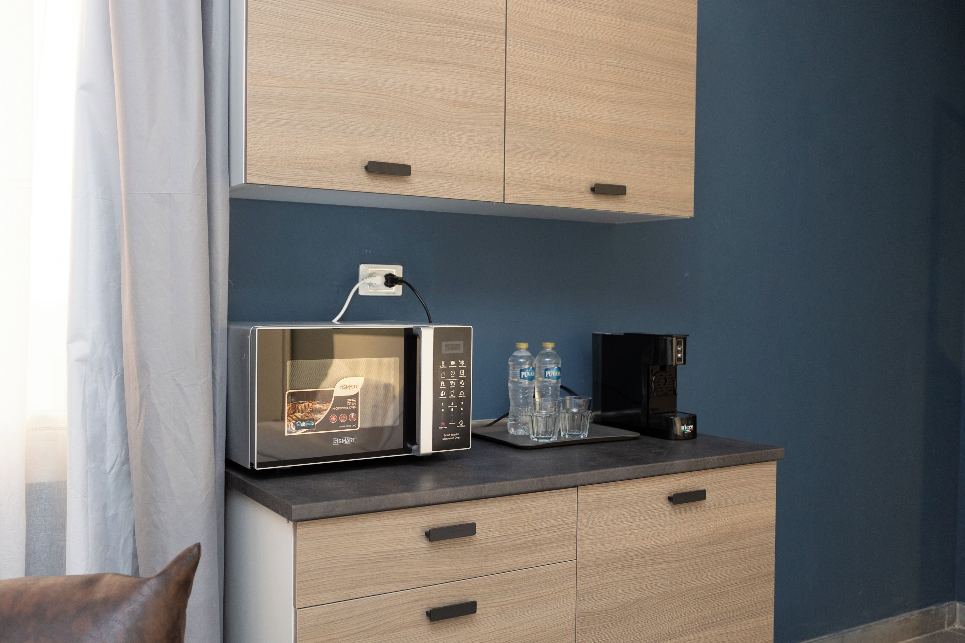 Una cucina moderna con forno a microonde integrato, macchina del caffè e dispenser d'acqua sul piano di lavoro.