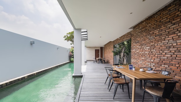 Ein moderner Essbereich im Freien mit Pool, Holzterrasse und Backsteinwand.
