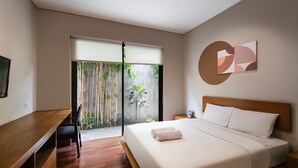 Ein modernes Hotelzimmer mit einem Holztisch, einem Bett mit weißen Leinentüchern, einem großen Fenster mit Blick auf Bambuspflanzen und einem an der Wand hängenden abstrakten Kunstwerk.