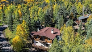 A large log cabin with a sloped roof, surrounded by dense forest with autumn foliage. - Vail Hideaway - Forest Views, Deck & Comfort (Vail)