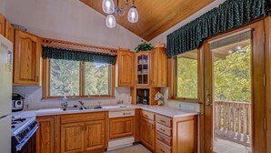 A kitchen with wooden cabinets, a stove, a sink, and a window with a view of trees. - Vail Hideaway - Forest Views, Deck & Comfort (Vail)