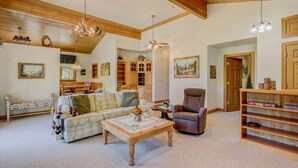 A spacious living room with a wooden ceiling, a sofa, a chair, a coffee table, and a bookshelf. - Vail Hideaway - Forest Views, Deck & Comfort (Vail)