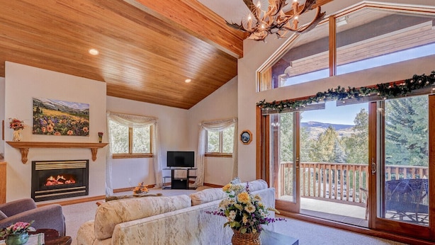 A spacious living room with a fireplace, comfortable seating, a television, and a balcony with a scenic view. - Vail Hideaway - Forest Views, Deck & Comfort (Vail)