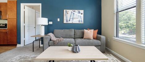 A living room with a grey sofa, a coffee table, a lamp, and a painting on the wall.