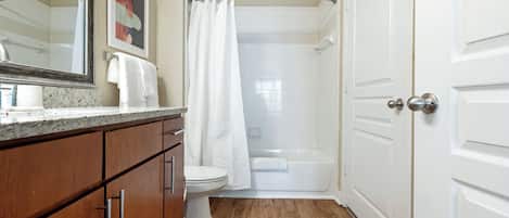 Une salle de bain avec un meuble-lavabo en bois, des toilettes blanches, une douche avec une porte en verre et une porte blanche.