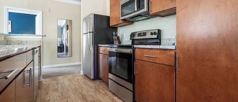 A modern kitchen with stainless steel appliances, wooden cabinets, and a granite countertop.