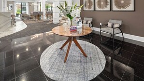 A lobby with a round table, chairs, a vase with flowers, and framed artwork on the wall. -  Landing Furnished Apartments - Charlotte Northlake (Charlotte)