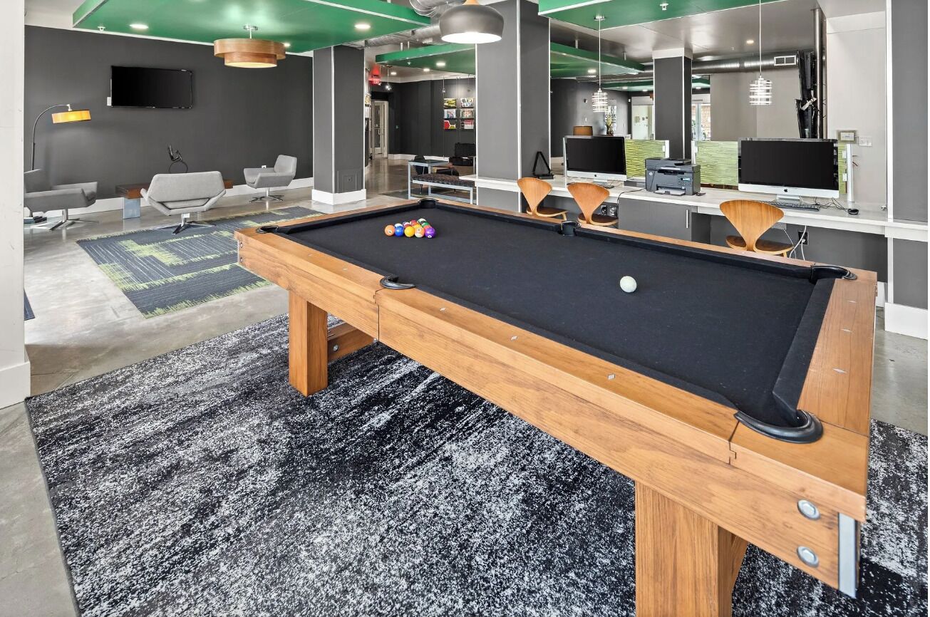 Una mesa de billar con estructura de madera y fieltro negro, rodeada de sillas modernas y un tapete de diseño blanco y negro.