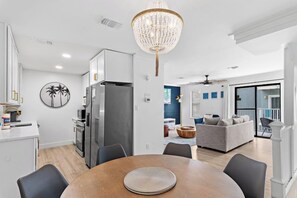 Una cocina moderna con comedor, una araña y un salón con sofá y balcón.