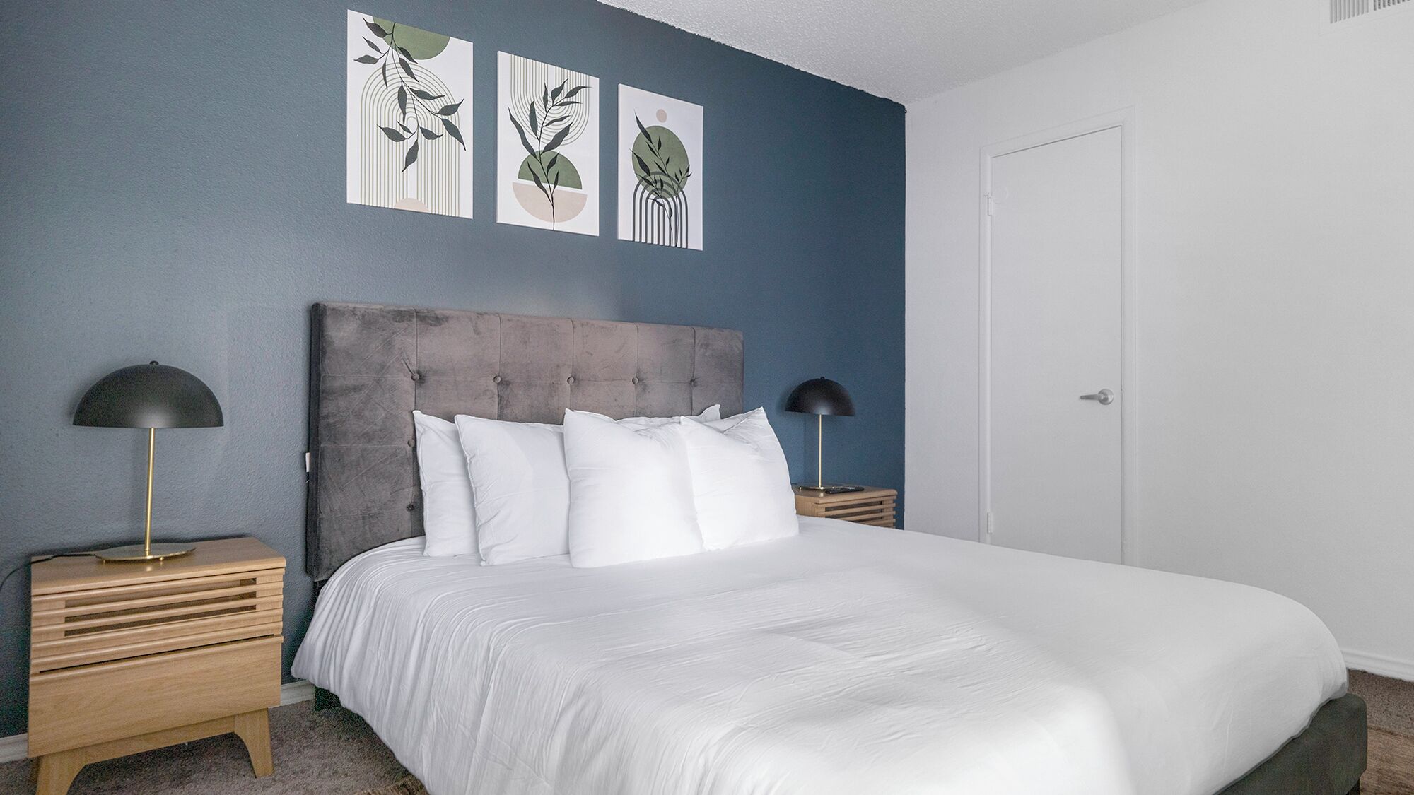 A bedroom with a large bed, two bedside tables, and three wall-mounted artworks.