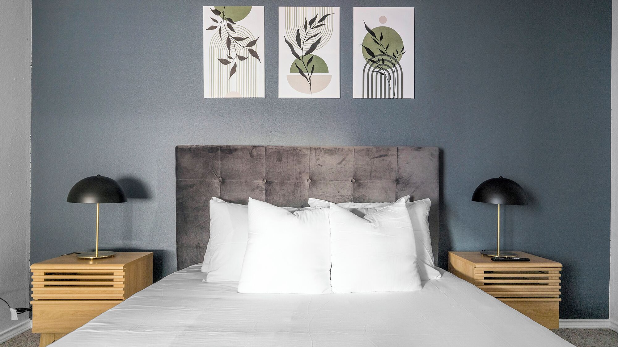 A bedroom with a large bed, two nightstands, and three wall-mounted artworks.