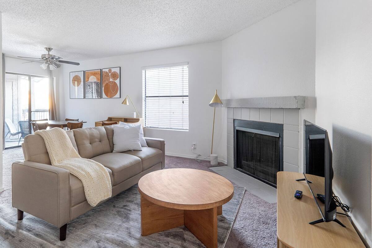 Un salon avec un canapé beige, une table basse ronde en bois, une cheminée et un ventilateur de plafond.