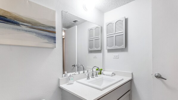 A modern bathroom with a white sink, a mirror, and a painting on the wall.