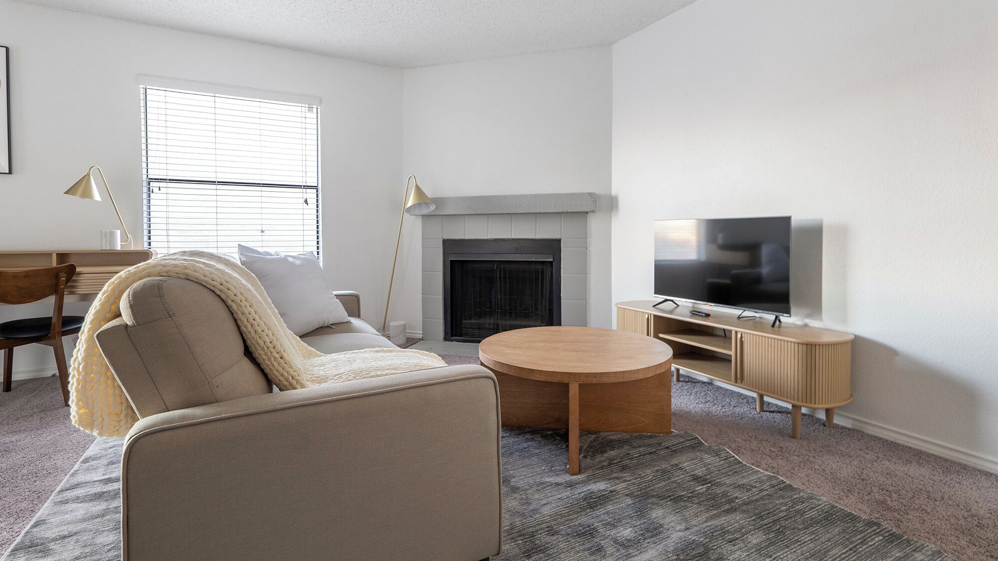 Ein Wohnzimmer mit einer Couch, Couchtisch, Fernseher, Kamin und einem Schreibtisch mit Lampe.